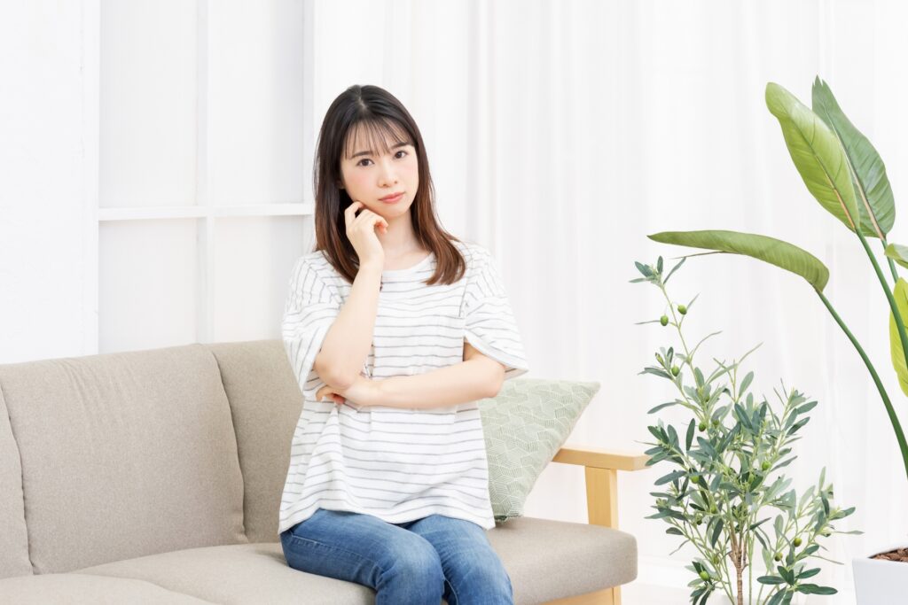 部屋のソファーに座って考え事をする若い女性